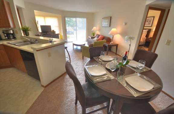 the dining room and living room of a condo with a dining table and a kitchen