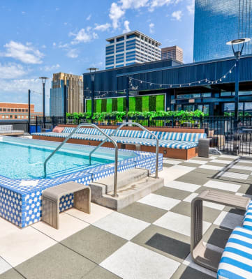 a rooftop pool with blue and white lounge chairs and a city skyline in the background