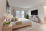 A virtual staged bedroom with a large window, and carpeted floors.