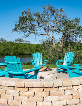 a fire pit with three adirondack chairs and a lake in the background