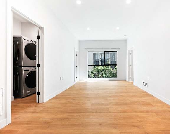 A long hallway with a washer and dryer on the left and a doorway leading to a balcony.