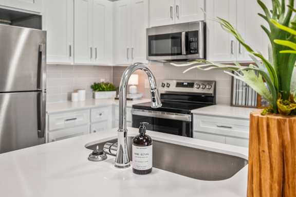 A kitchen with a stainless steel refrigerator, a white sink, and a wooden vase with a plant.