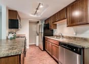 Thumbnail 12 of 26 - Pet-Friendly Apartments in Aurora, CO - Copper Flats - Kitchen with Plank Flooring, Granite-Style Countertops, Dark Wood Cabinetry, Stainless Steel Appliances, and Laundry Room with In-Unit Washer and Dryer.