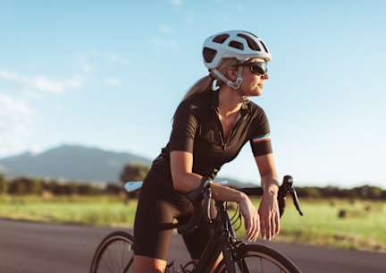 A woman wearing a helmet and sunglasses is riding a bicycle.
