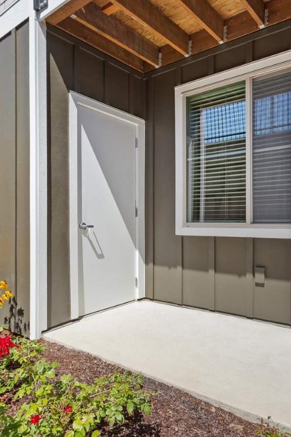 A white door is open to a small patio with a flower bed.