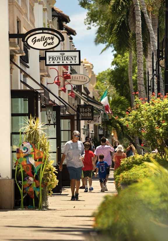 a group of people walking down a sidewalk in front of shops