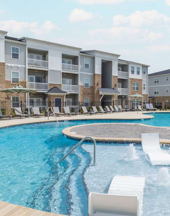 a large swimming pool with lounge chairs and umbrellas in front of an apartment building
