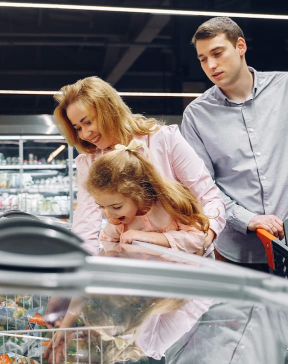 a family of three looking at a shopping cart in a grocery store