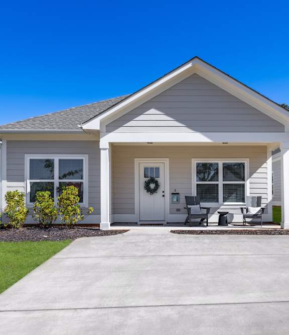 A cottage with large windows, front porch, and two-car driveway