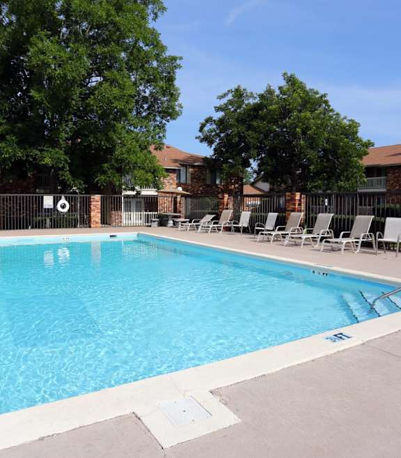 A swimming pool surrounded by a white border and lounge chairs.