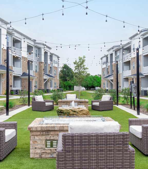 an outdoor lounge area with chairs and a fire pit in front of an apartment complex