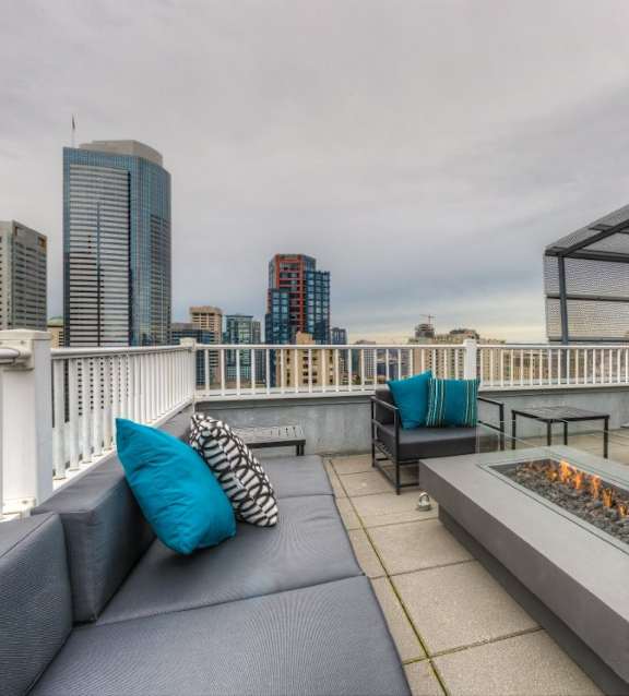A modern outdoor seating area with a fire pit and city skyline in the background.