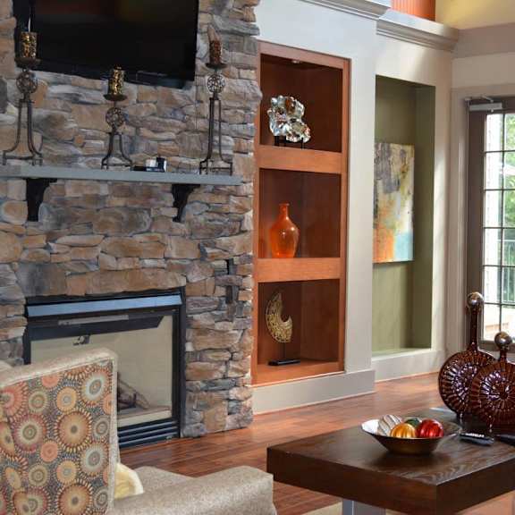 A living room with a stone fireplace and a chair with a patterned cover.at Riverview Landing @ Valley Forge, Eagleville Pennsylvania