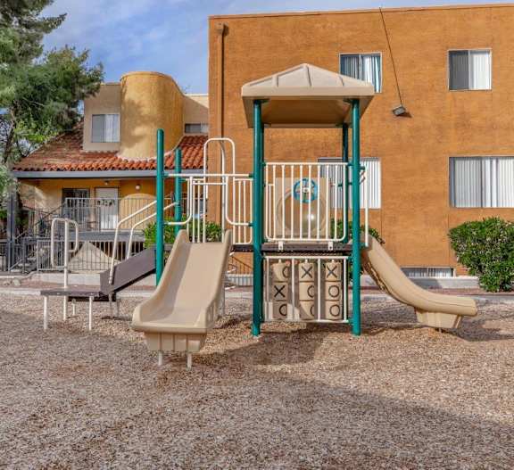 A playground with a slide and a swing set in front of a building.