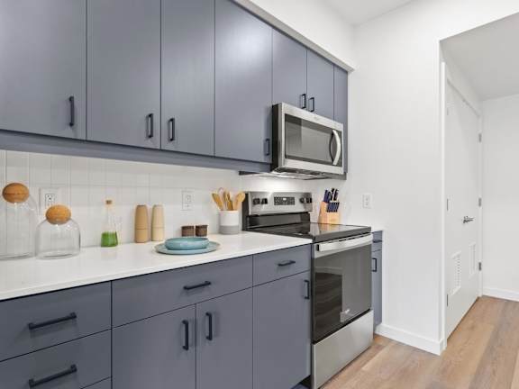 A kitchen with grey cabinets and a white countertop.