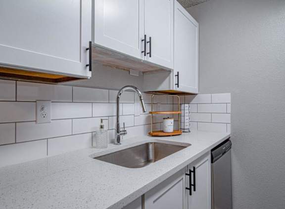 A kitchen with a white counter top and a stainless steel sink.