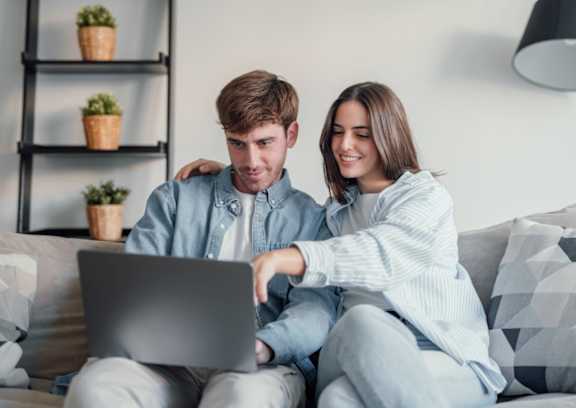 A man and woman are sitting on a couch with a laptop.