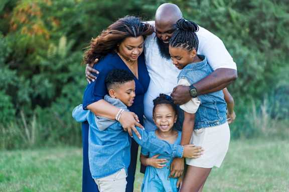A family of four hugging each other in a field.