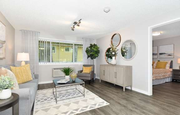 A well-lit living room with a grey couch, a coffee table, and a large mirror on the wall.