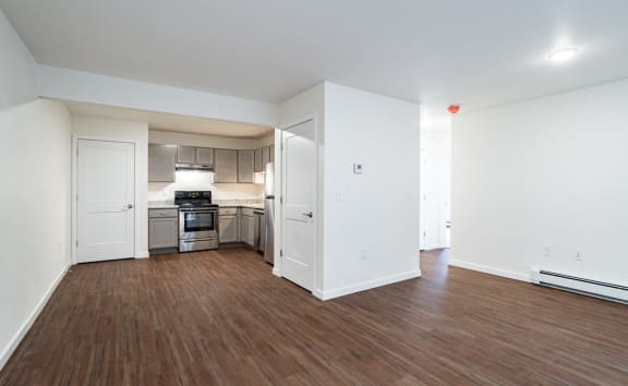 an empty living room and kitchen with wood flooring and white walls