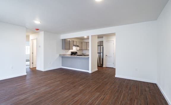 an empty living room with wood flooring and a kitchen