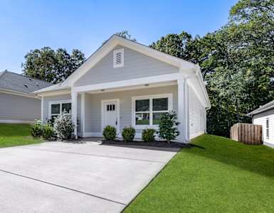 A light grey cottage with a large front porch, private backyard, and two-car driveway