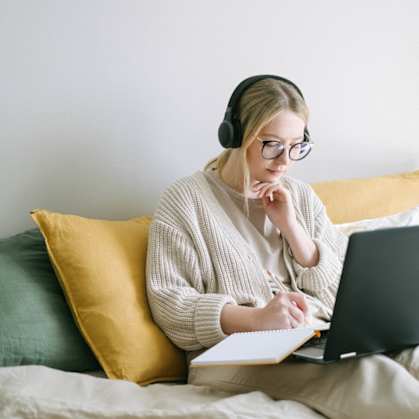 a woman sitting on a bed with a laptop and headphones on
