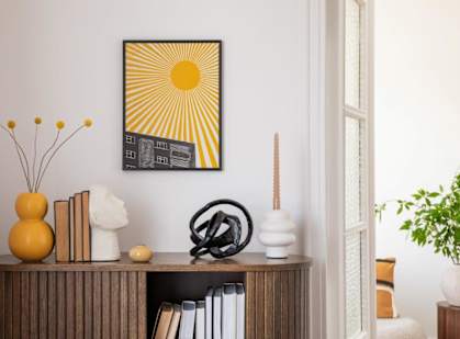 A sunny yellow picture hangs on a wall above a shelf with books and decorative objects.