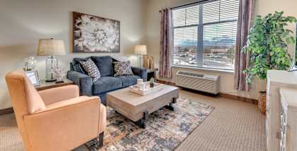A living room with a blue couch, a chair, a coffee table, and a large window with a view of the city.