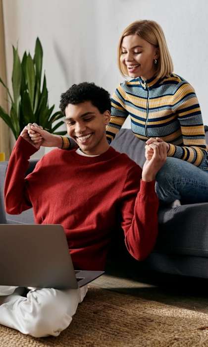 A man and woman are sitting on a couch with a laptop on the floor in front of them.