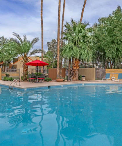 A swimming pool surrounded by palm trees and red umbrellas.