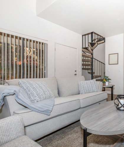 A living room with a grey couch, a round table, and a ceiling fan.
