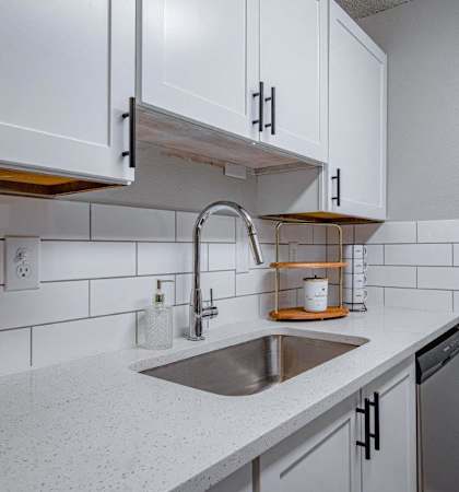 A kitchen with a white counter top and a stainless steel sink.