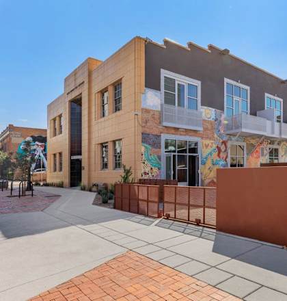 A building with a mural on the side has a red fence in front of it.