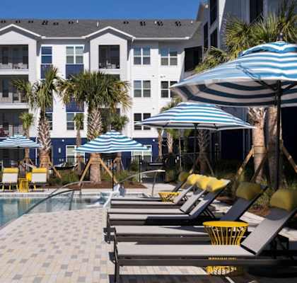 A pool area with sun loungers and umbrellas in front of a white building.