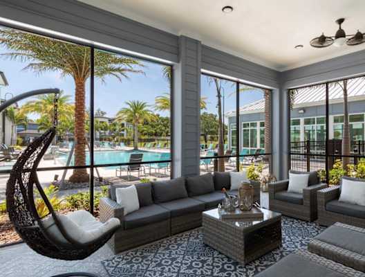 A modern outdoor living space with a hanging chair and a pool in the background at The Addison on Long Bayou Apartments, Seminole, Florida