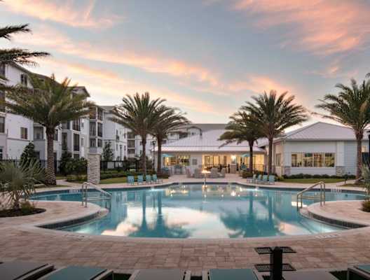 A large swimming pool surrounded by palm trees and a building in the background. at Enclave at 3230 Apartments, South Daytona, 32119