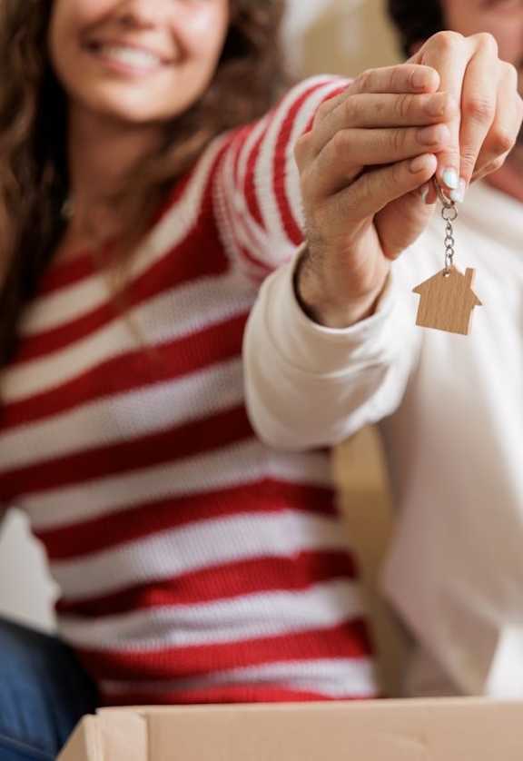 A man in a white hoodie is holding a key with a house-shaped keychain.