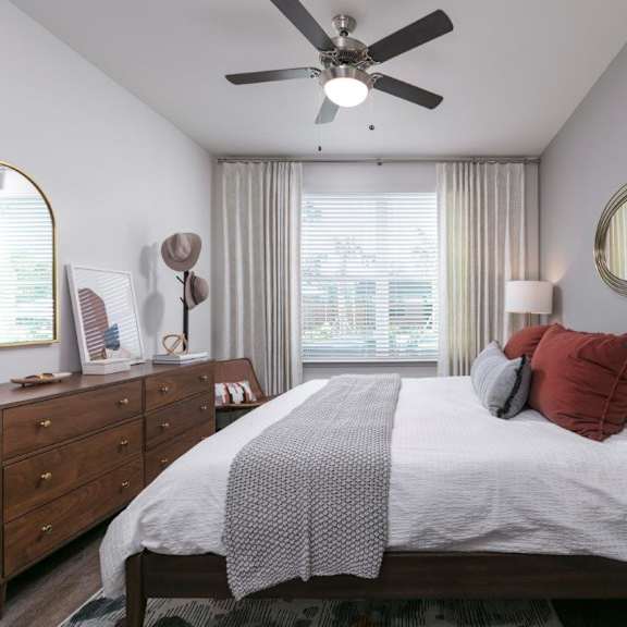 A bedroom with a large bed, a ceiling fan, and a window with curtains.