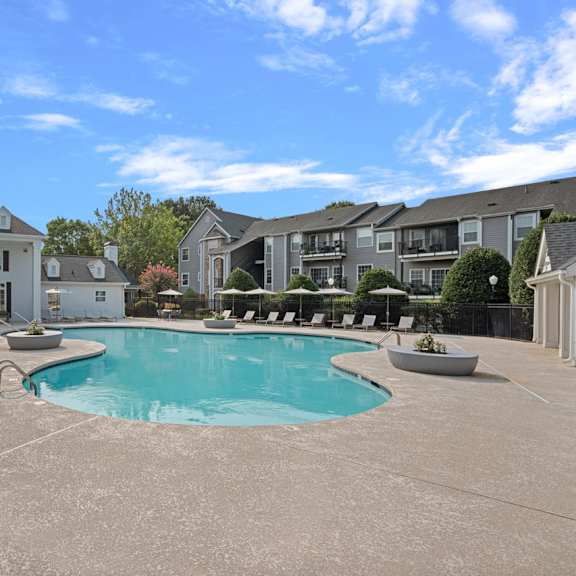 A large swimming pool is surrounded by a concrete patio and lounge chairs.
