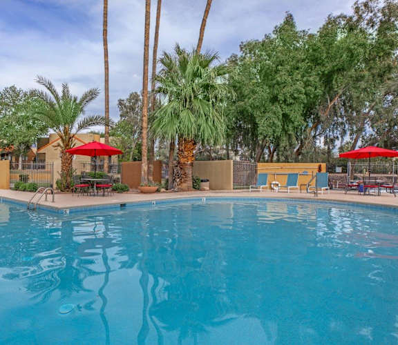 A swimming pool surrounded by palm trees and red umbrellas.