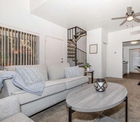 A living room with a grey couch, a round table, and a ceiling fan.