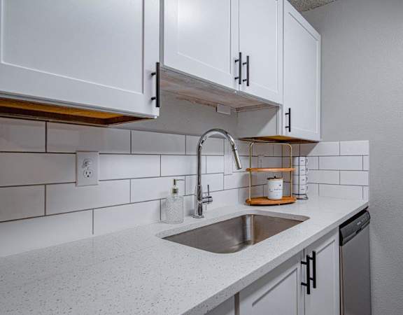 A kitchen with a white counter top and a stainless steel sink.
