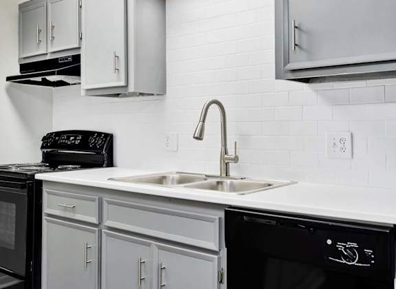 A modern kitchen with a black microwave, black oven, and black toaster on a white countertop.