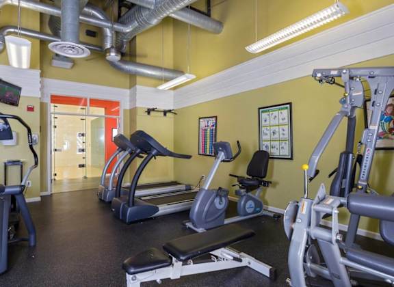 a gym with cardio equipment and weights in a building with yellow walls at Village Club of Royal Oak, Royal Oak, 48067