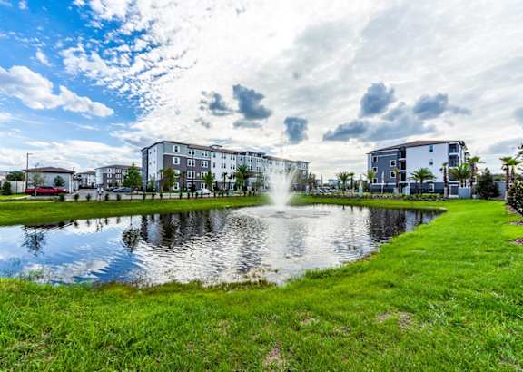 A fountain in the middle of a grassy area with buildings in the background.