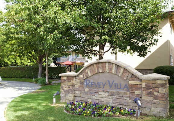 a stone sign that says in front of trees and flowers