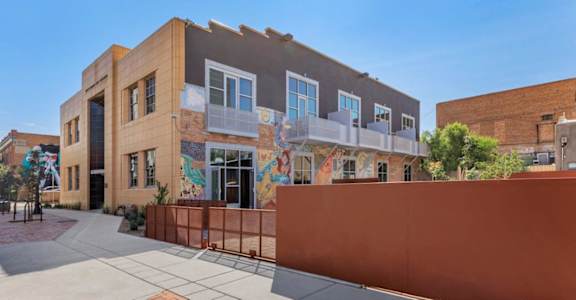 A building with a mural on the side has a red fence in front of it.
