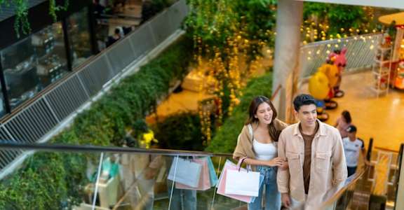 A couple is standing on an escalator in a shopping mall.