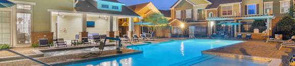 A large swimming pool in front of a building with a sunset in the background. at Audubon Park Apartment Homes, Zachary, LA